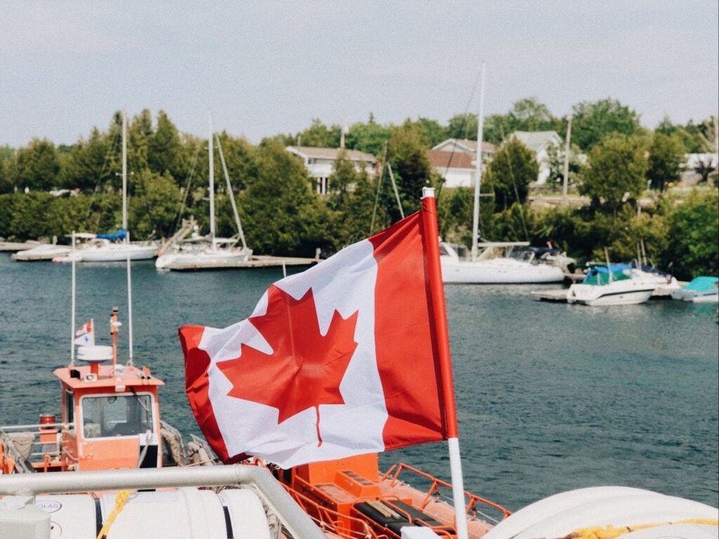 A vibrant Canadian flag waving at a harbor with boats nearby during a summer day.