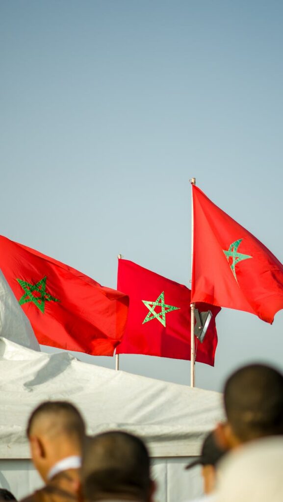 Three Moroccan flags with star emblem waving at an outdoor event with clear sky background.